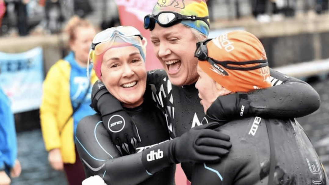 Three swimmers hugging and smiling
