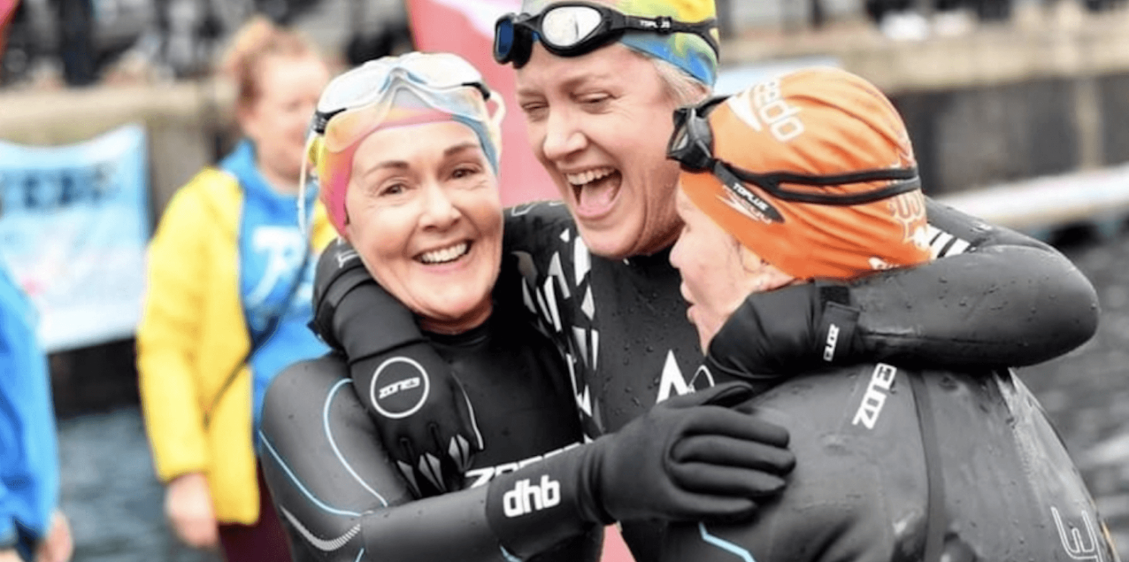 Three swimmers hugging and smiling